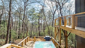 A wooden deck with a hot tub and grill, surrounded by a forest. - BRAND NEW Modern Luxe Scandinavian Cabin with Hot tub/Fire Pit WIFI (Blue Ridge)