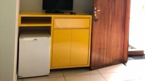 Ένα δωμάτιο με ένα κίτρινο γραφείο, μια τηλεόραση και ένα μικρό λευκό ψυγείο.