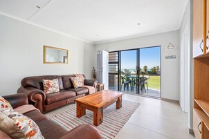 A spacious living room with a brown leather sofa, a wooden coffee table, and a large sliding glass door leading to an outdoor area.