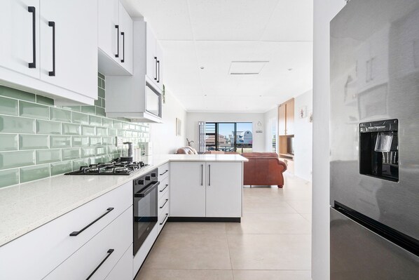 A modern kitchen with white cabinets, a green-tiled backsplash, and a stainless steel refrigerator.