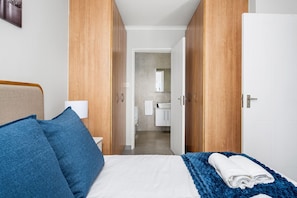 A hotel room with a bed, blue pillows, a white blanket, and a blue throw. - Rouxvilla (Jeffreys Bay)