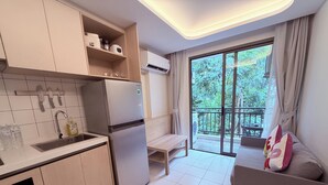 A modern kitchen with a refrigerator, sink, and cabinets, a balcony with a table and a sofa, and a large window with a view of greenery. - The best vacation at Kamala Beach! Pool, gym, shuttle bus .511 (Tambon Kamala)