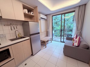 A modern kitchen with a refrigerator, sink, and cabinets, a balcony with a table and a sofa, and a large window with a view of greenery. - The best vacation at Kamala Beach! Pool, gym, shuttle bus .511 (Tambon Kamala)