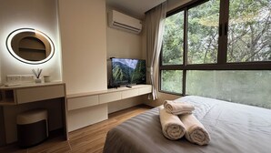 A hotel room with a bed, a TV on a stand, a desk with a mirror, and a window with a view of trees. - The best vacation at Kamala Beach! Pool, gym, shuttle bus .511 (Tambon Kamala)
