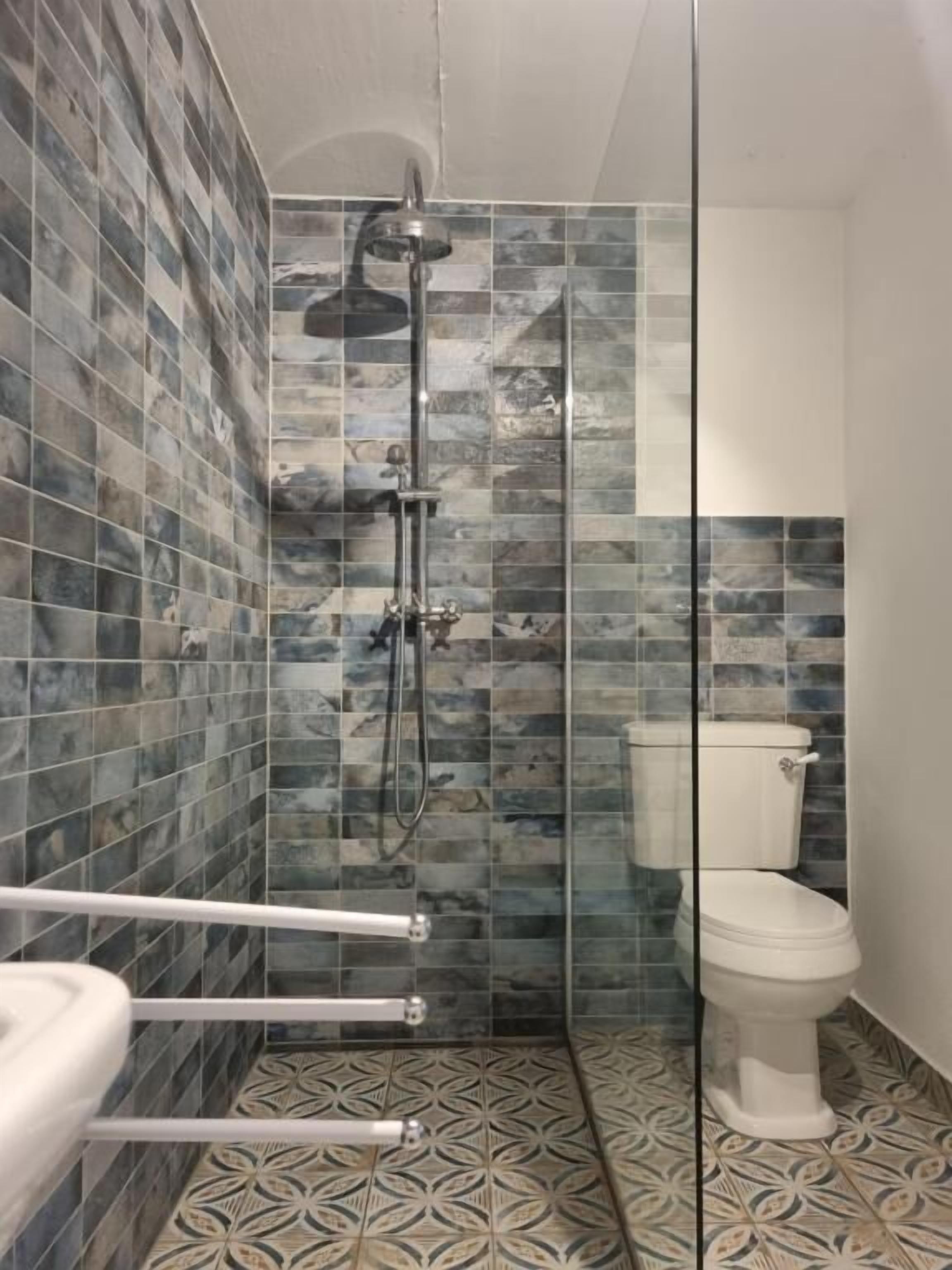A bathroom with a shower, toilet, and patterned floor tiles.
