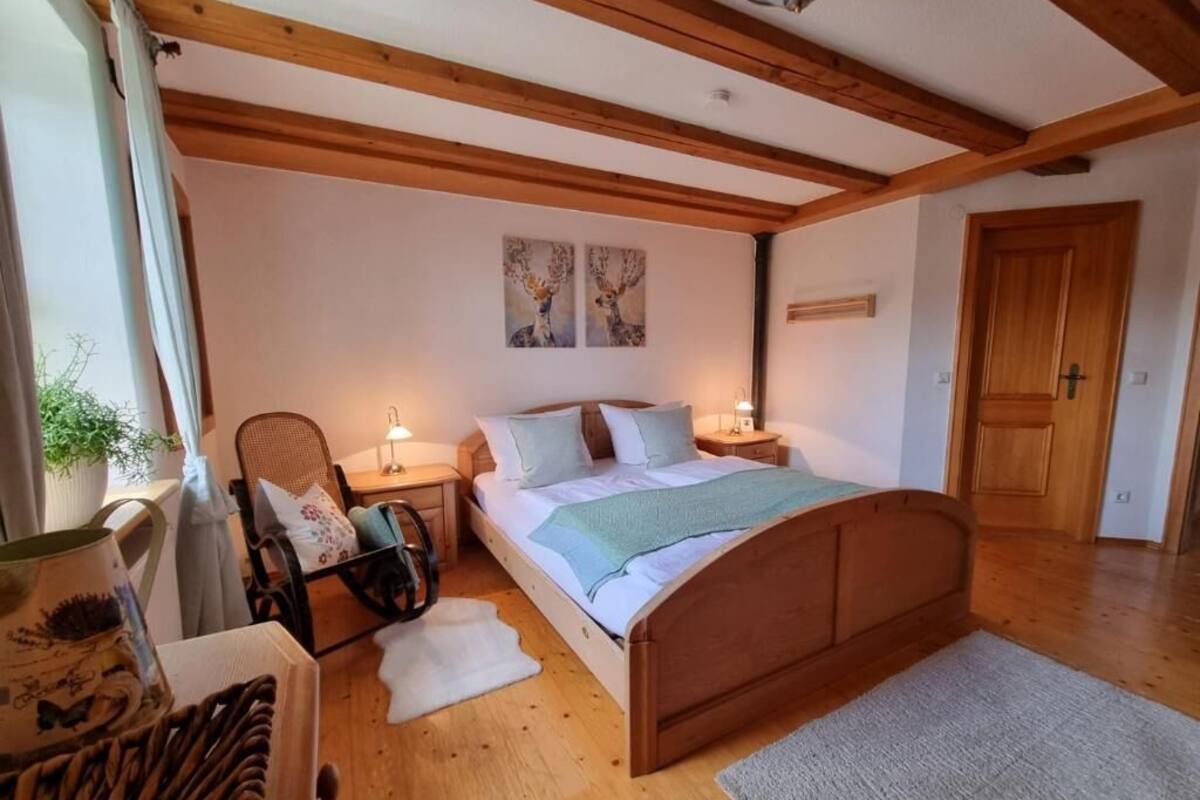 A bedroom with a wooden bed, two bedside tables, a chair, a rug, and a door.