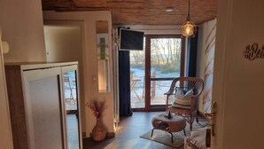 Un pasillo con techo de madera, una silla de mimbre, un televisor y vistas al exterior.