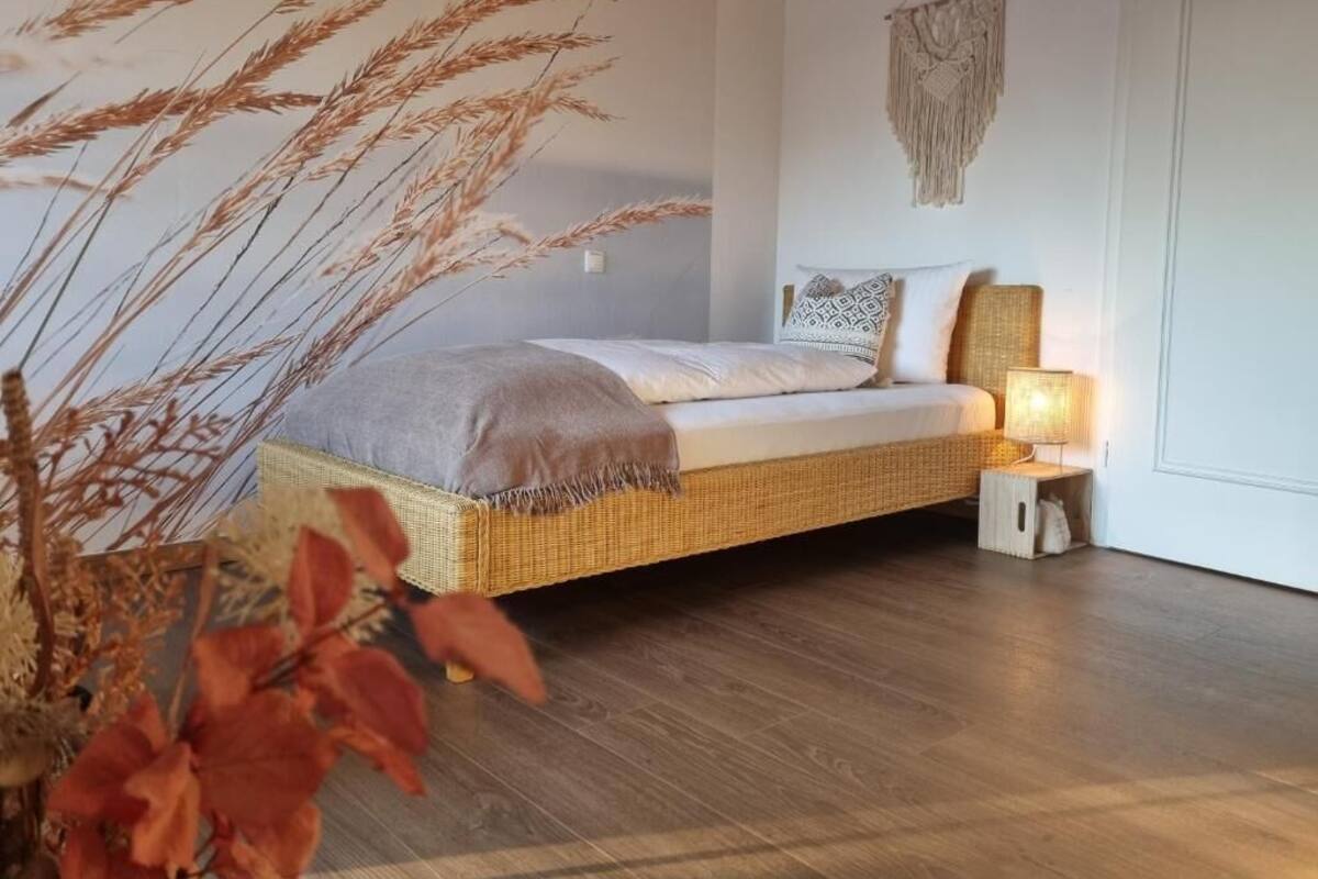 A bedroom with a wicker bed, a bedside lamp, and a macrame wall hanging.