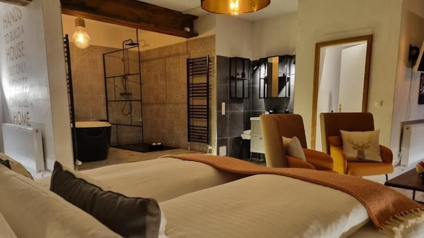 Habitación de hotel con cama, sillón, escritorio, espejo y zona de ducha.