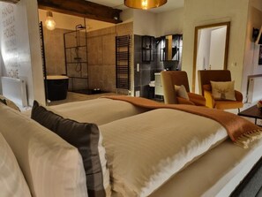 Habitación de hotel con cama, sillón, escritorio, espejo y zona de ducha.