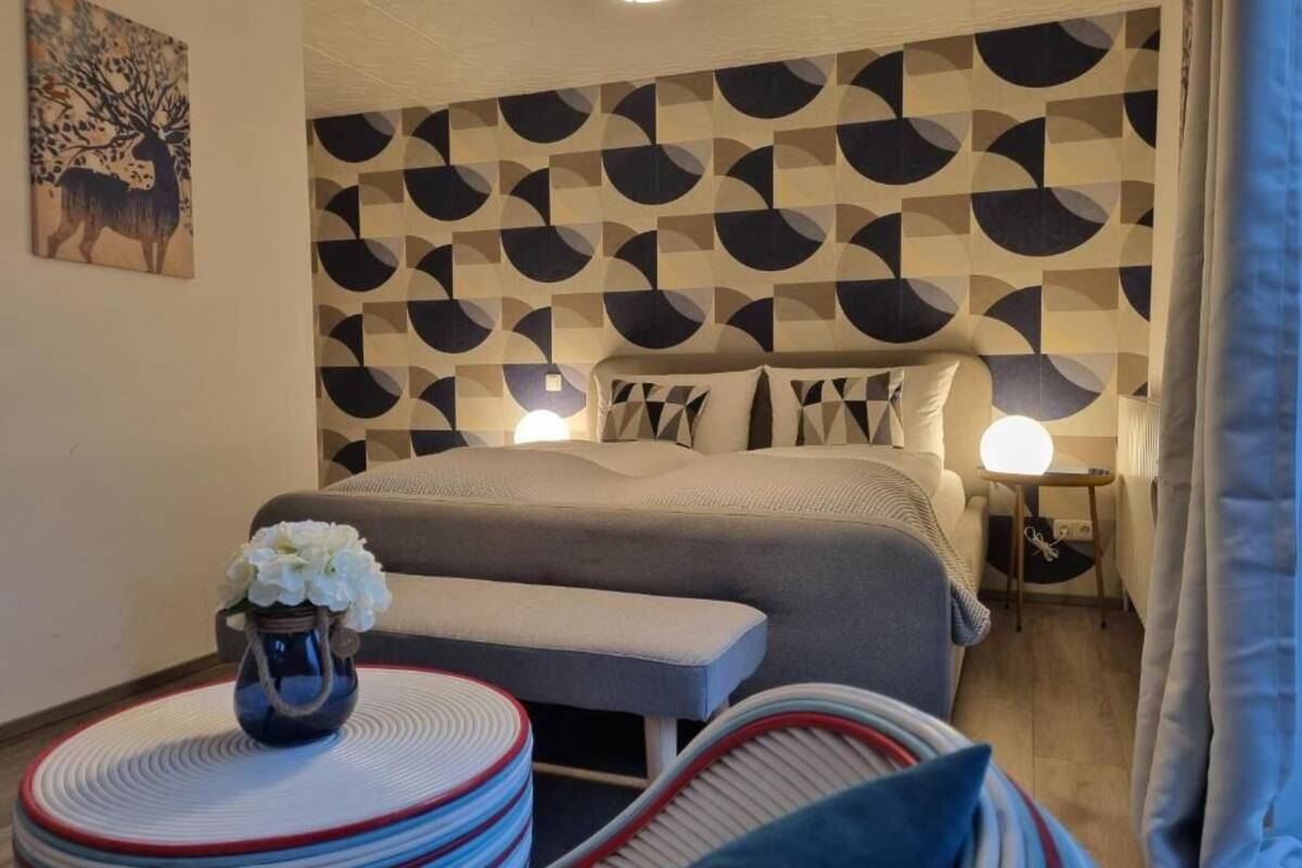 A bedroom with a patterned headboard, a bed with pillows, bedside tables, and a vase with flowers.