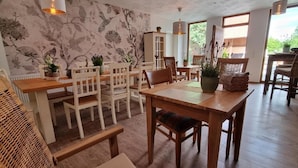 Un comedor con mesas y sillas de madera, plantas en macetas y un papel tapiz floral.