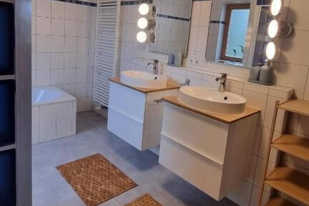 A modern bathroom with two sinks, a mirror, and a ceiling light.