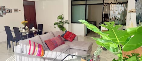 A modern living room with a grey sectional sofa, a glass coffee table, and a dining area with a table set for four.