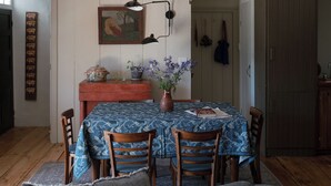 Zona pranzo con tavolo apparecchiato per quattro, sedie in legno, un vaso con fiori e un quadro appeso al muro.