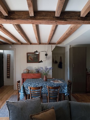 Un coin repas avec une table dressée pour quatre personnes, des chaises en bois, un vase rempli de fleurs et un tableau accroché au mur.