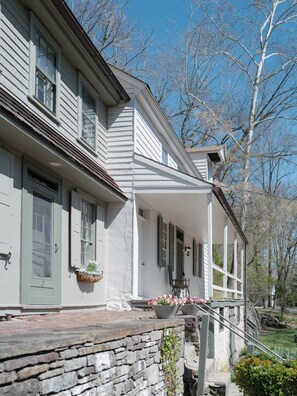 Une maison à deux étages, avec des fondations en pierre, un porche abrité et un petit jardin.