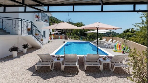 Ein Pool auf dem Dach mit Liegestühlen und Sonnenschirmen, umgeben von einem weißen Gebäude mit einem Balkon.