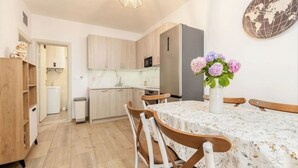 Eine kompakte Küche mit Holzausbau, einer Mikrowelle und einem Kühlschrank. Es gibt einen Esstisch mit Stühlen und eine Blumenvase.