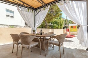 Eine möblierte Terrasse im Freien mit Korbmöbeln und einem Tisch, umgeben von weißen Vorhängen.