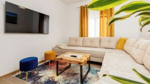 Ein modernes Wohnzimmer mit einer Couch, einem Couchtisch, einem an der Wand befestigten Fernseher und einem Fenster mit Vorhängen.