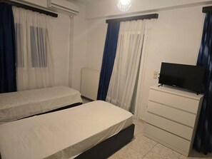 A bedroom with two beds, a TV on a dresser, and a radiator. - Charming Apartment with Ocean and Garden Views, 1km from the beach in Greece (Messini)