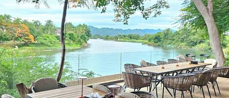 Een terras buiten met een tafel en stoelen, met uitzicht op een rivier en begroeiing.