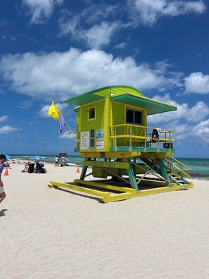 Una torre de salvavidas con techo verde y detalles amarillos en una playa arenosa.