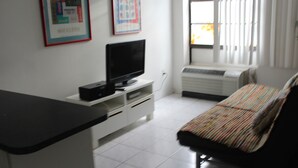 Ein Zimmer mit einem Bett, einem Fernseher auf einem Schrank, einer weißen Klimaanlage und einem Fenster mit Jalousien.