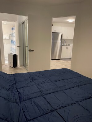 Ein Schlafzimmer mit einem großen Bett, ein Badezimmer mit Dusche und eine Küchenzeile mit Kühlschrank.