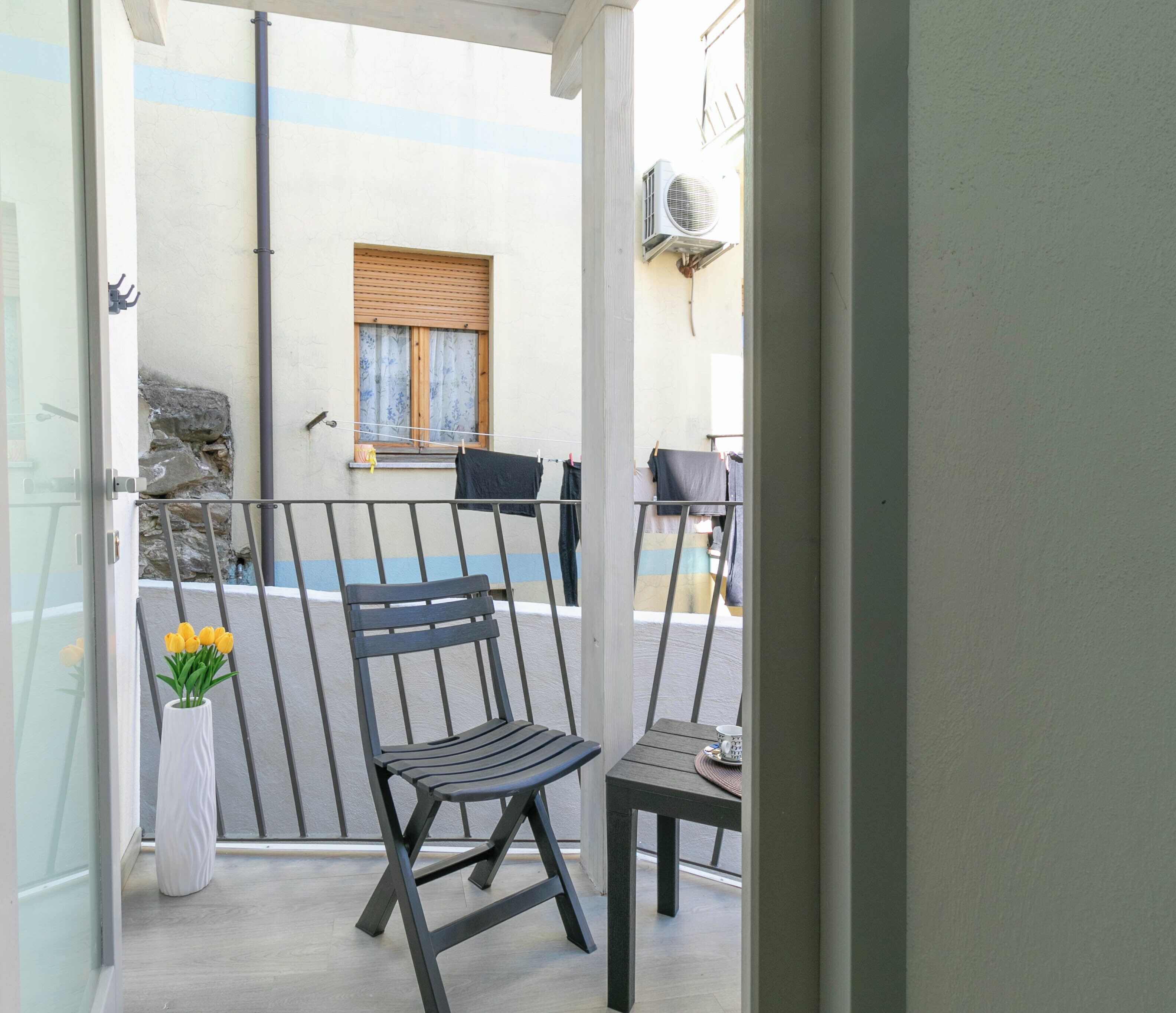Un balcon avec deux chaises, une petite table et un pot de fleurs.