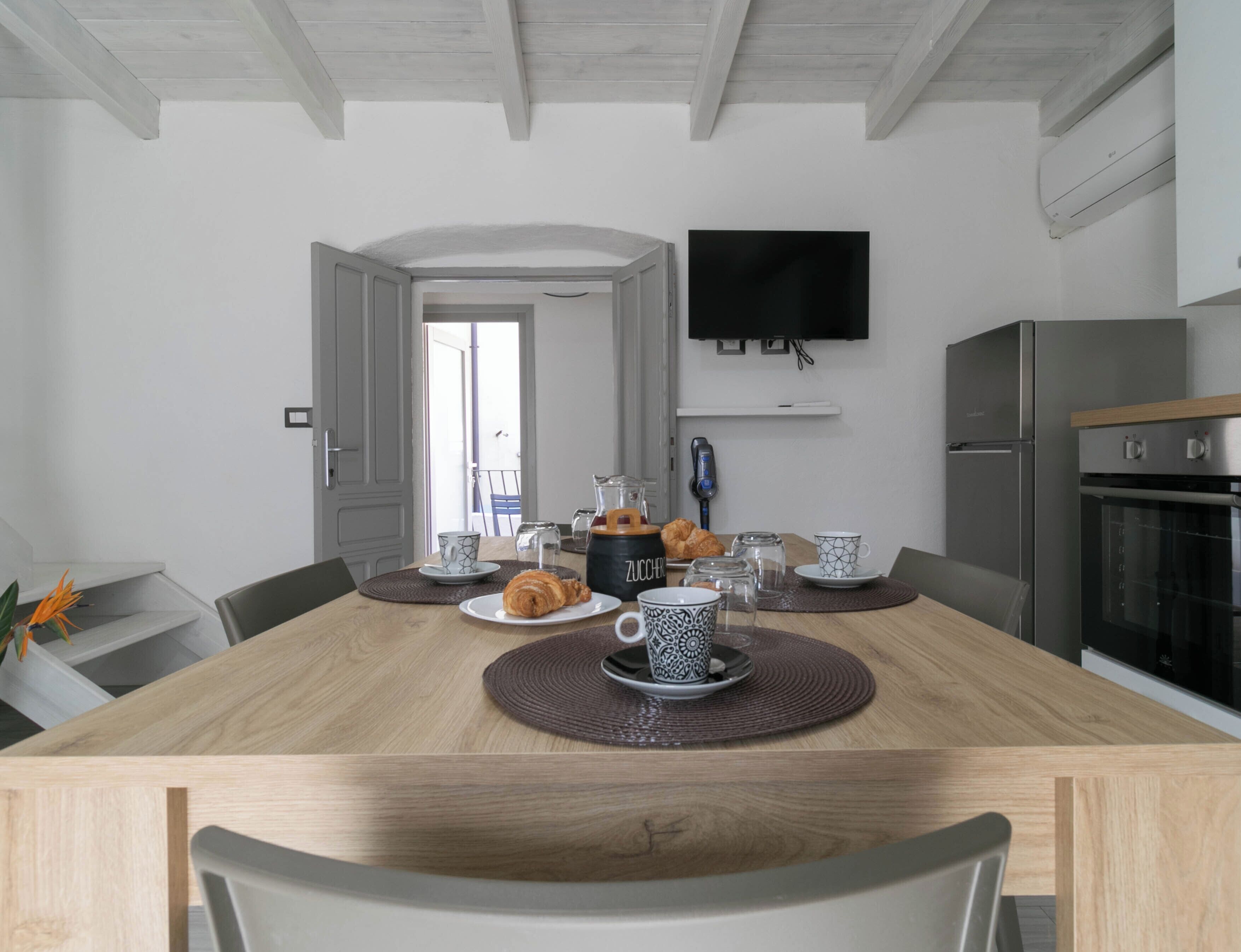 Eine moderne Küche mit Esstisch, Stühlen, einem an der Wand montierten Fernseher und einem eingebauten Backofen.