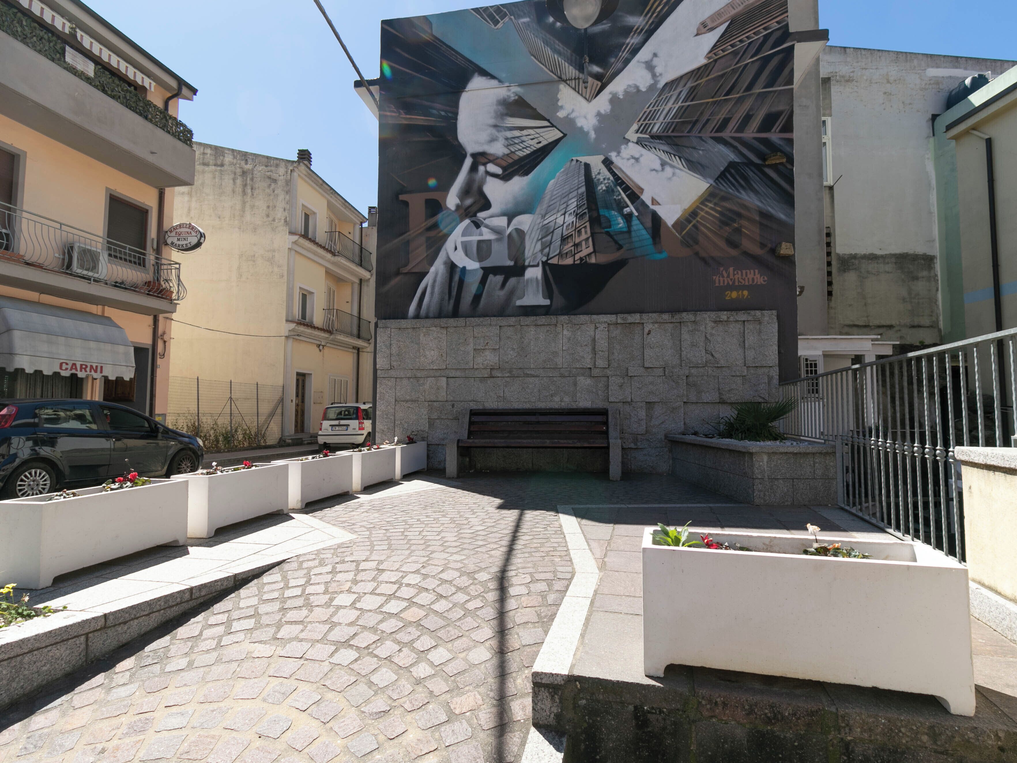 Una calle con un mural grande, una zona pavimentada y un banco.