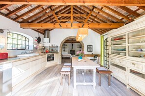 A spacious kitchen with wooden beams, a central island, and a dining area with a table and benches.