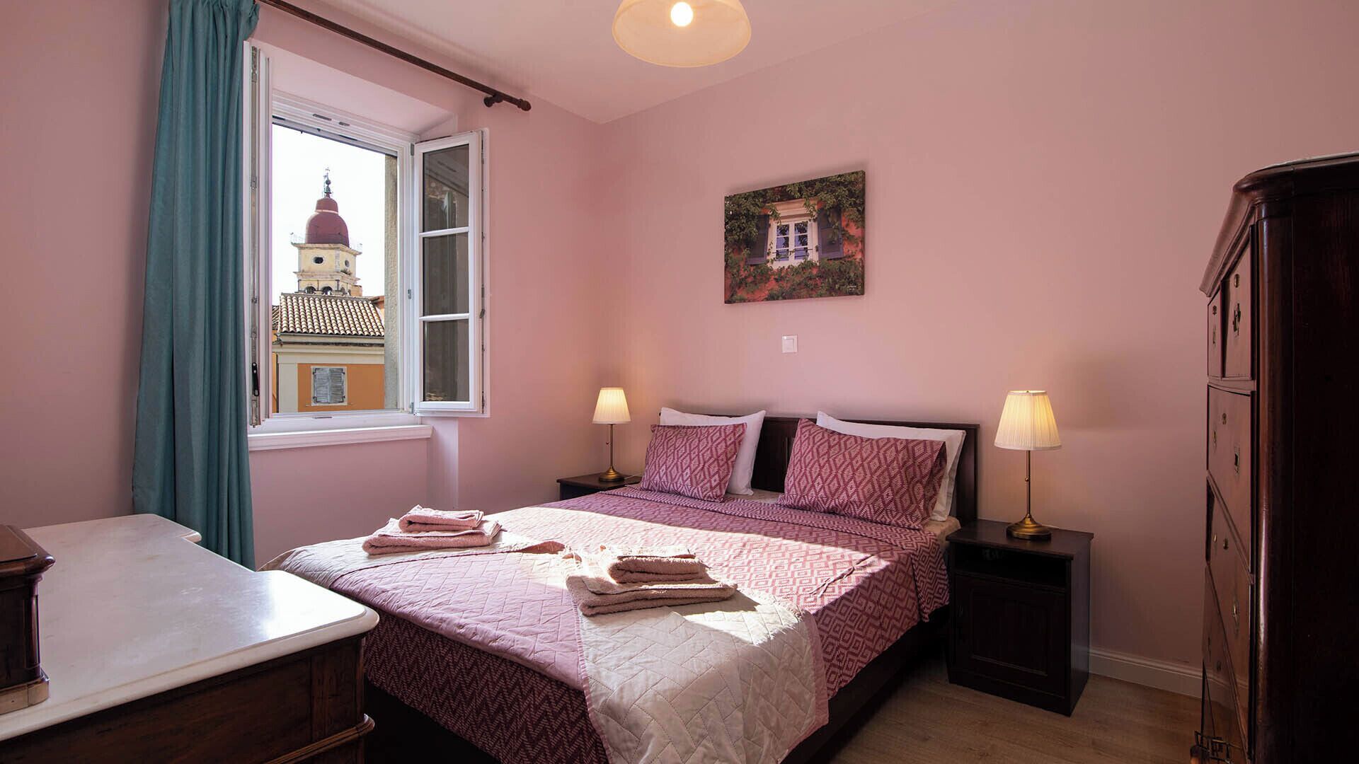 Ein Schlafzimmer mit einem Bett, zwei Nachttischen, einem Schreibtisch, einem Kleiderschrank, einem Fenster mit Vorhängen und einem Gemälde an der Wand.