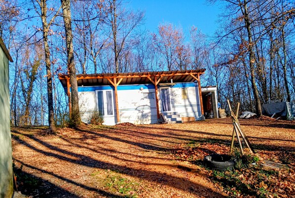 Eine kleine Holzhütte mit einer Holzterrasse, umgeben von Bäumen und einem klaren Himmel.