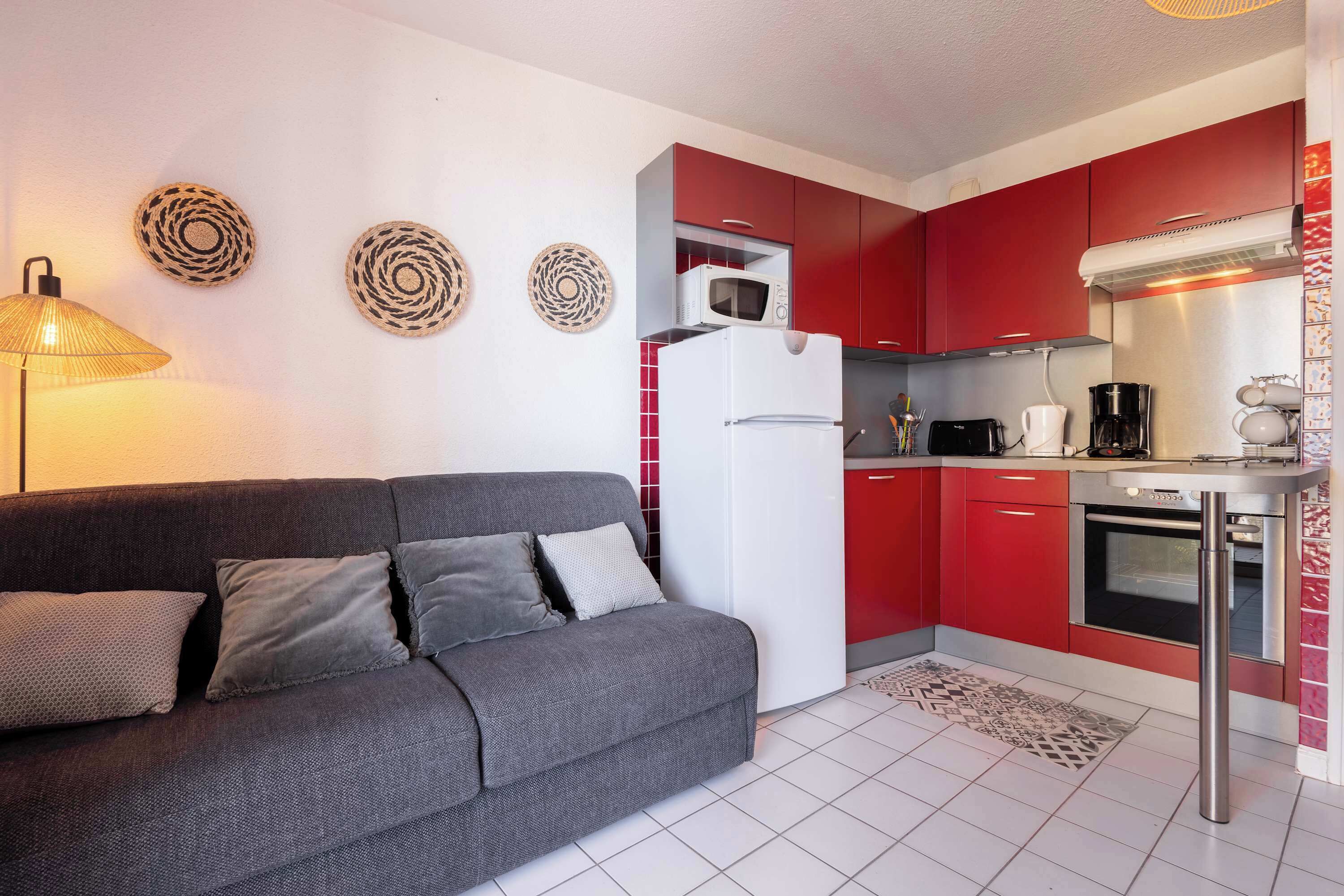 A modern kitchen with red cabinets, a white refrigerator, and a coffee maker.