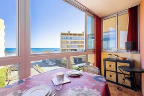 A balcony with a table set for dining, a wicker chair, and a view of the sea and buildings. - Valras-Plage  Appartement avec Vue Mer (Valras-Plage)