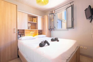 A neatly made bed with two rolled towels, a bedside lamp, and a window with curtains. - Valras-Plage  Appartement avec Vue Mer (Valras-Plage)