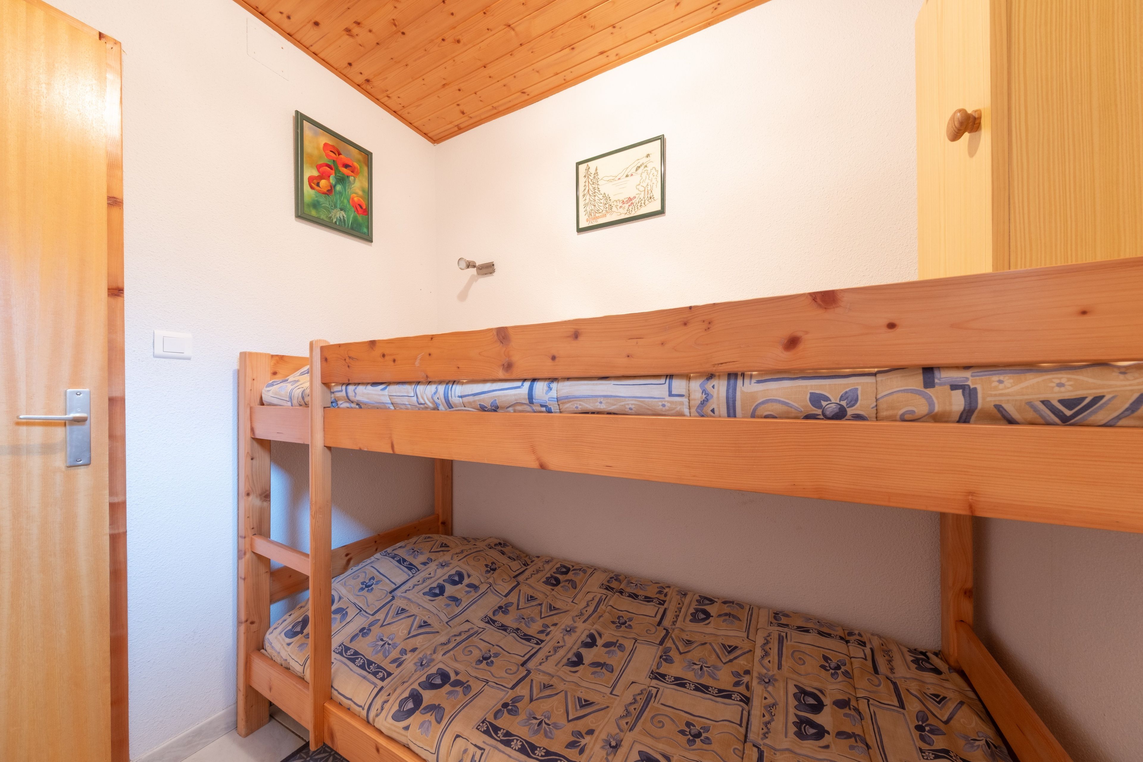 Una cama litera con ropa de cama estampada, una puerta de madera y dos cuadros en la pared.