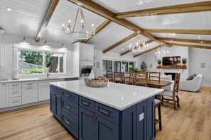 A modern kitchen with a large island, wooden beams, and a dining area with a TV above the fireplace. - Award-Winning Resort Amenities | 2404 Waterway by Wild Dunes (Isle of Palms)
