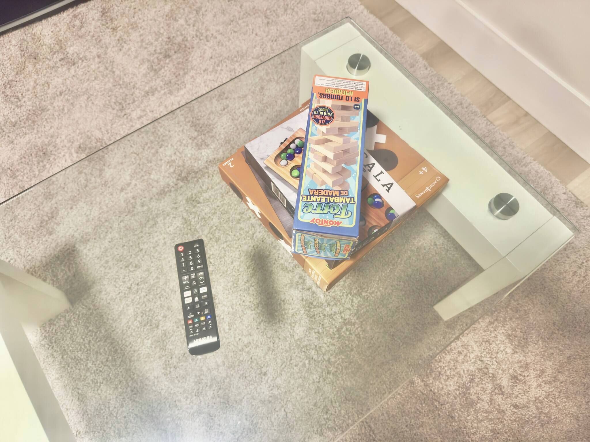 Une télécommande, une pile de livres et un jeu de cartes sur une table en verre.