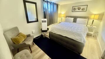 Una habitación de hotel con cama, lámparas de noche, un calentador, una silla, una mesita y un espejo.