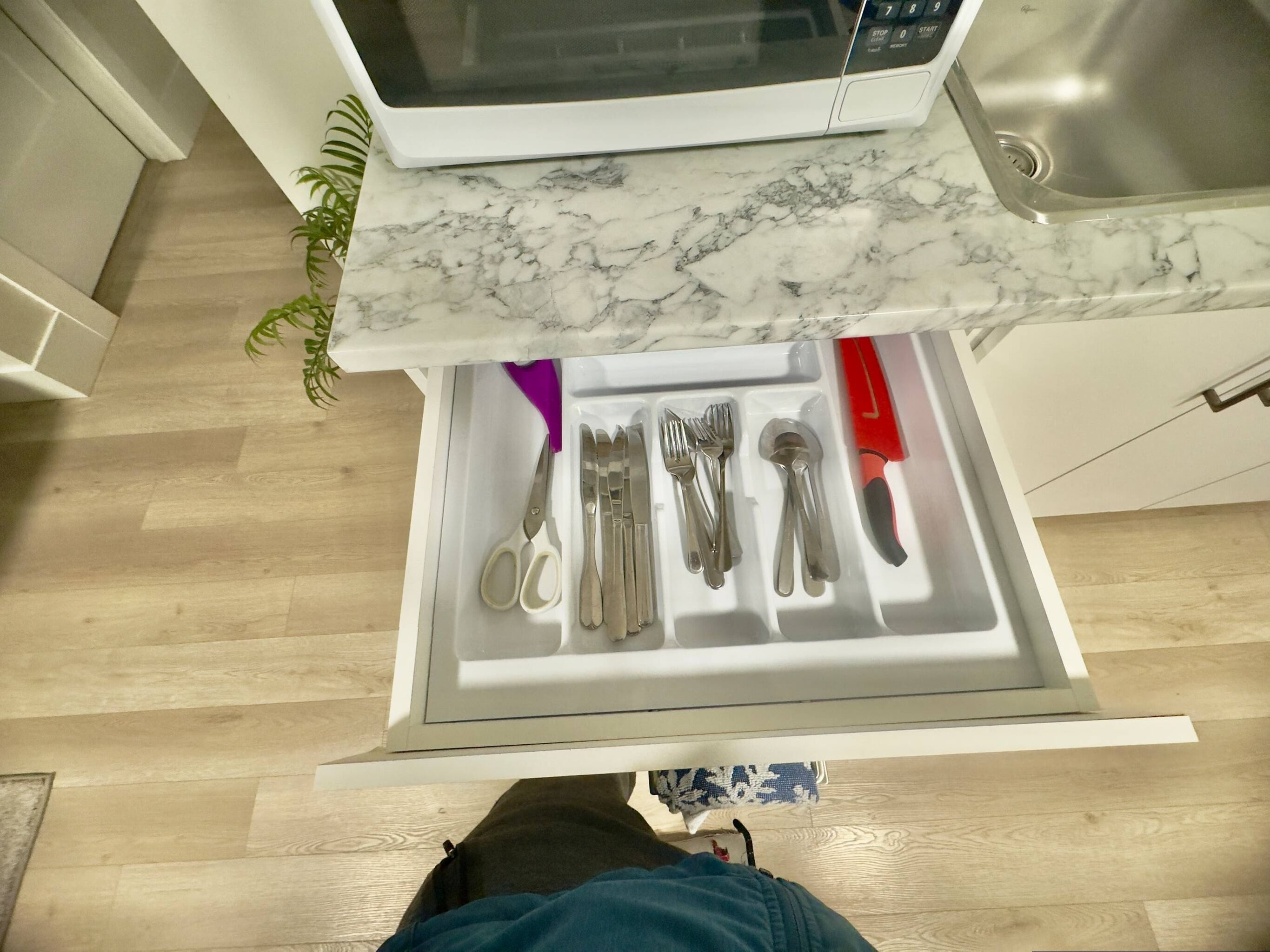 Una cocina con un microondas, un cajón con utensilios y una planta.