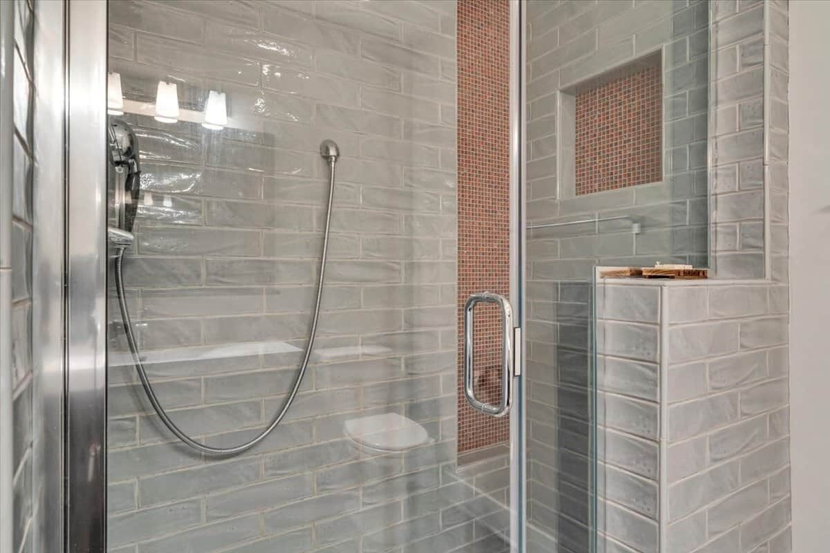 A glass-enclosed shower with a metal handle, a glass partition, and a tiled wall with a brick pattern.
