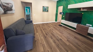 A living room with a sofa, a flat-screen TV, and a green accent wall. - A stone's throw from the sea and the heart of the city (Livorno)
