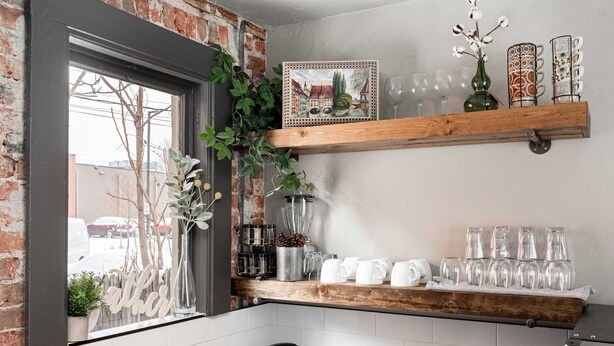 Een keuken met een bakstenen muur, een raam met beplanting en planken met keukengerei en decoratieve objecten.