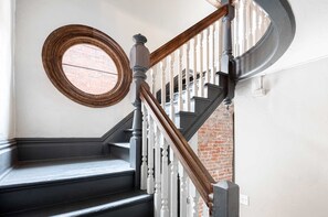 A staircase with white balusters, a wooden handrail, and a circular window. - Vibrant Tennyson Victorian | 96 Walk Score | 30Day (Denver)
