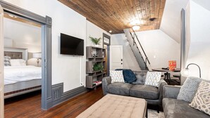Een slaapkamer in loftstijl met een groot bed, een televisie, een trap en een zithoek met een bank en een salontafel.