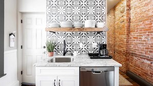 Een keuken met witte kastjes, een marmeren aanrechtblad, een bakstenen muur en een decoratieve spatwand.